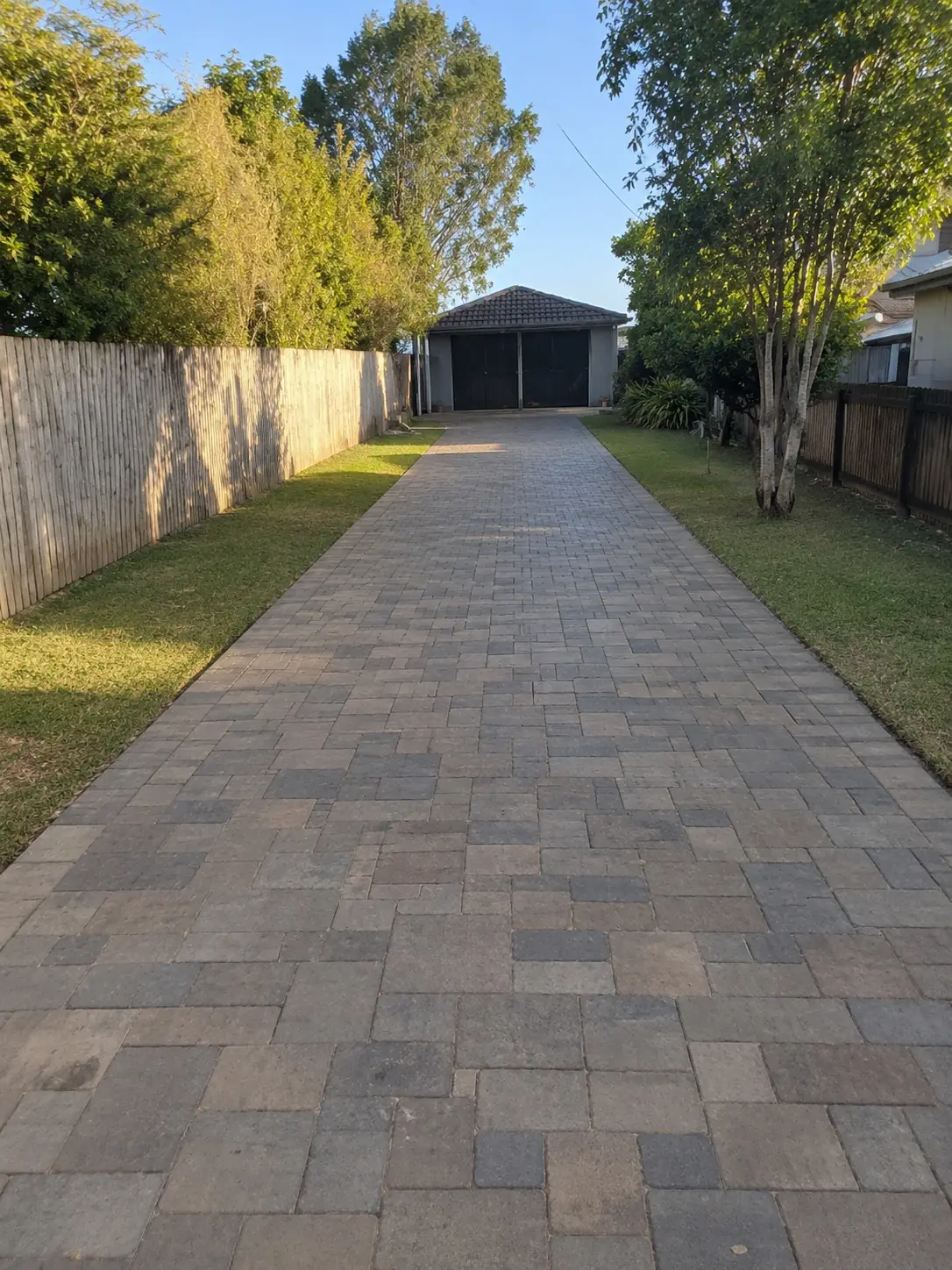 Paver driveway stretching past green lawns to a garage at the back of a Darwin block